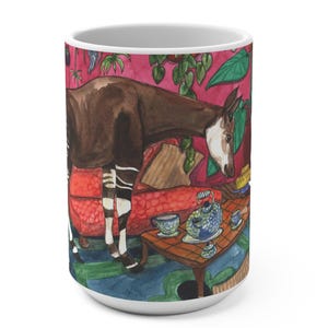 Könnte beinhalten: Weiße Keramiktasse mit einer Aquarellillustration eines Okapi in einem Raum mit rotem Sofa und Teeservice. Das Okapi hat braun-weiß gestreifte Beine und einen braunen Körper. Der Hintergrund ist eine rosa Wand mit grünen Pflanzen.