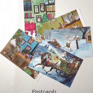 May include: A collection of whimsical postcards featuring watercolor illustrations of rabbits in various winter and holiday scenes. The postcards showcase scenes with reindeer, sleighs, and snowy landscapes. The word "Postcards" is printed at the bottom.
