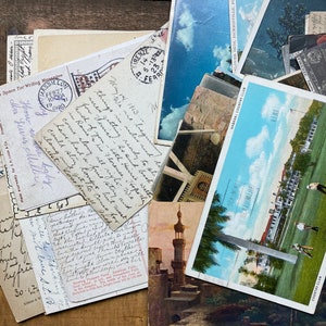 May include: A collection of vintage postcards featuring various scenes, including a cityscape, a country club, and a mosque. The postcards are arranged on a wooden surface and some have handwritten messages on the back.