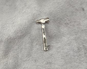 以下が含まれることがあります： ハンマーの形をした小さな銀色の金属製チャーム。ハンマーは丸みを帯びたヘッドと湾曲したハンドルが特徴で、ベース部分にはチェーンやコードに取り付けるための小さな穴が開いています。表面は磨き上げられた光沢のある仕上げです。