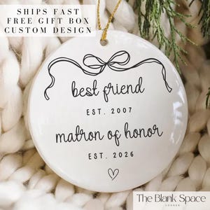 May include: White ceramic ornament with black script reading "best friend" and "matron of honor", with the years 2007 and 2026. A bow design is at the top. The text "SHIPS FAST FREE GIFT BOX CUSTOM DESIGN" is at the top.