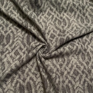 May include: Close-up of a gray fabric with a repeating cable knit pattern. The fabric is soft and draped, with a swirling texture. The color is a mix of light and dark gray, creating depth and dimension. This textile is suitable for apparel or home decor.