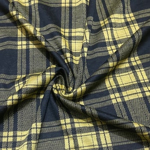 May include: Black and gold plaid fabric with a woven texture. The fabric is folded and draped, showing the pattern and texture.