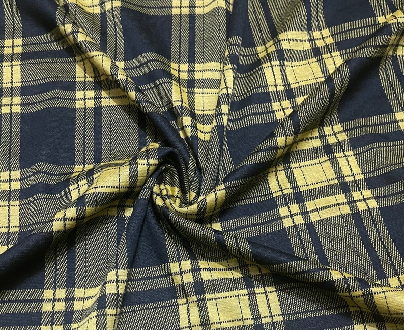 May include: Black and gold plaid fabric with a woven texture. The fabric is folded and draped, showing the pattern and texture.