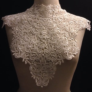 May include: White lace collar with a delicate floral pattern. The collar is made of a soft, lightweight fabric and has a scalloped edge.