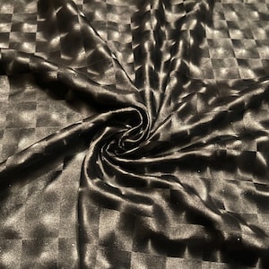 May include: Black fabric with a checkered pattern. The fabric has a shiny, satin-like appearance and is draped in soft folds. The pattern is a repeating grid of squares, creating a textured effect. The fabric is suitable for clothing or home decor.