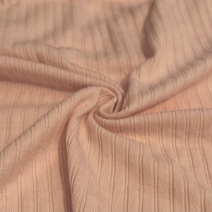 May include: Close-up of a soft, light pink ribbed knit fabric. The fabric is folded and swirled, showcasing the vertical ribbing pattern. The texture appears smooth and slightly stretchy, ideal for clothing.