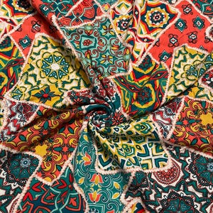 May include: A fabric textile featuring a repeating patchwork pattern of geometric and floral shapes in vibrant shades of coral, teal, mustard yellow, and white. The material is gathered in the center, creating folds that highlight the intricate design.