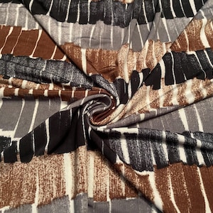 May include: Close-up of a fabric with a repeating pattern of vertical brushstrokes in shades of brown, black, gray, and white. The fabric is folded and draped, showing the texture and design.