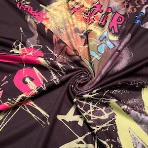 May include: Dark fabric with a graffiti-style design. The fabric features colorful text, abstract shapes, and splatters in shades of pink, yellow, blue, and orange against a dark background. The fabric is swirled.
