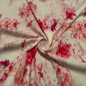 May include: White fabric with a repeating floral pattern of pink and red peonies. The fabric is folded, showing the texture and color variations of the flowers. The flowers have orange accents.