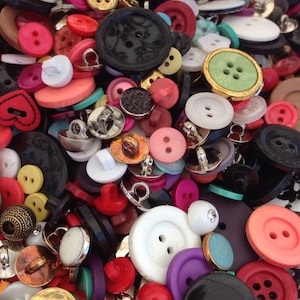 May include: A large collection of colorful buttons in various shapes and sizes. The buttons are made of plastic, metal, and fabric. Some buttons have a shiny finish, while others have a matte finish.