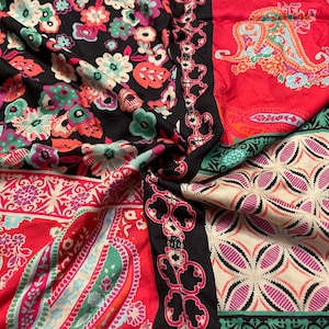 Può includere: Un tessuto colorato con motivi floreali e paisley. Il tessuto presenta uno sfondo nero con fiori nei toni del rosa, verde acqua e bianco. Altre sezioni hanno sfondi rossi e crema con motivi paisley e geometrici. Un bordo nero con un design floreale separa le sezioni.