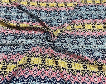 May include: Close-up of a patterned fabric with a repeating geometric design. The fabric features horizontal bands of navy blue, white, pink, and yellow. The pattern includes diamond and zigzag shapes, creating a textured appearance.