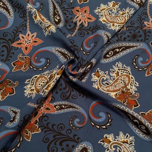 May include: A blue fabric featuring a repeating paisley pattern in shades of brown, orange, and cream. The design includes intricate swirling floral motifs and teardrop shapes printed across the surface, creating a dense and colorful textile.