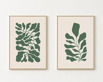 May include: Two framed wall art prints featuring dark green organic leaf shapes on a light beige background. The left print displays a dense, vine-like foliage pattern, while the right print shows a single, centered leafy stem. Text reads ABSTRACT ART SET OPAPERRIA PRINTS.