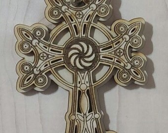 May include: A wooden ornament in the shape of a cross with intricate details. The cross is decorated with a swirling design in the center and has a string attached for hanging.