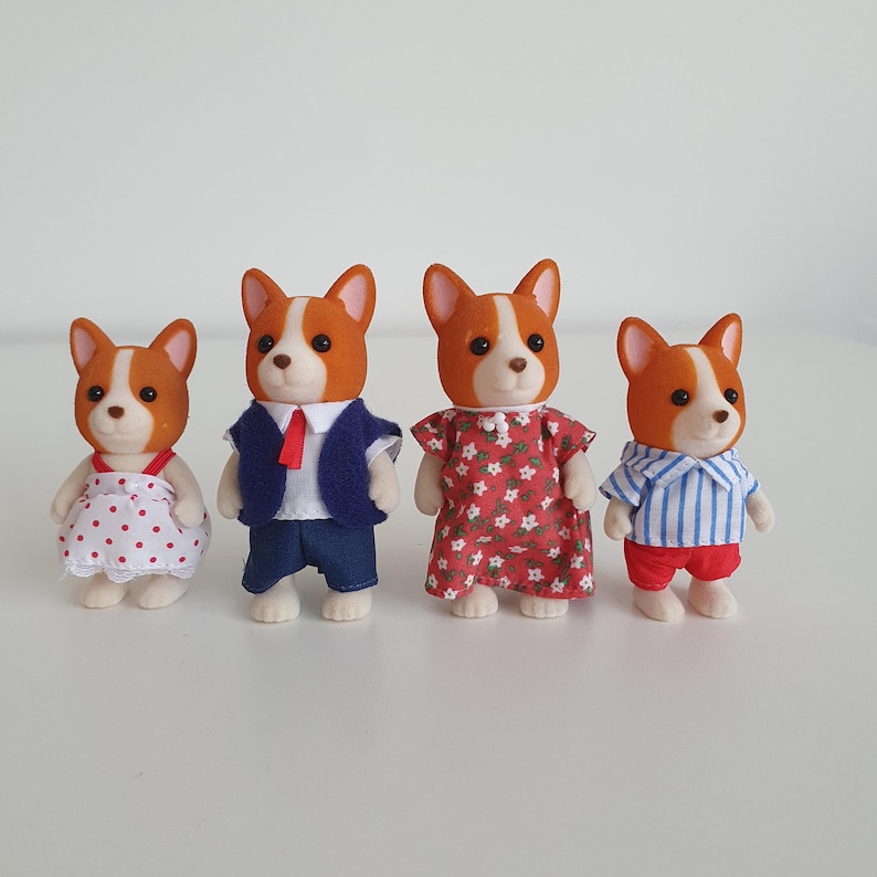 May include: Four miniature corgi figurines. The corgis are dressed in various outfits: a polka-dot dress, a suit with a red tie, a floral dress, and a striped shirt with red shorts. The corgis have brown and white fur.