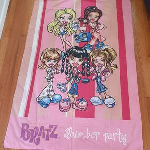 Puede incluir: Sábana rosa de Bratz "slumber party" con ilustraciones de dibujos animados de cinco muñecas Bratz con varios atuendos. La sábana tiene rayas rosas y blancas y las palabras "Bratz slumber party" en cursiva.
