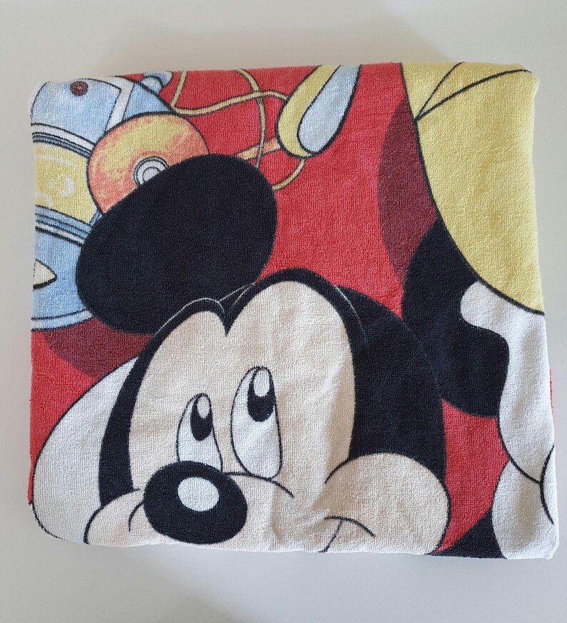 May include: Folded red and white Mickey Mouse towel. The towel features a large image of Mickey Mouse's face, with black, white, and red colors. The towel is made of a soft, absorbent material.