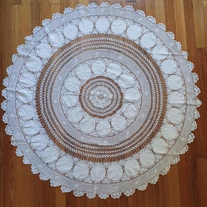 May include: A white crocheted tablecloth with a circular design featuring multiple layers of concentric circles and a central floral motif.