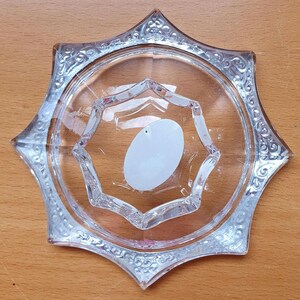 May include: A clear glass star-shaped dish with a decorative etched design around the edge. The dish has a smaller, raised star-shaped section in the center.