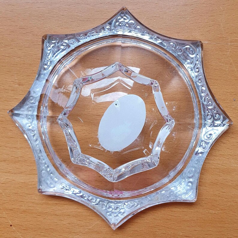 May include: A clear glass star-shaped dish with a decorative etched design around the edge. The dish has a smaller, raised star-shaped section in the center.