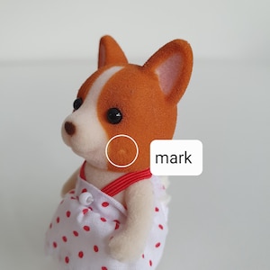 May include: A miniature dog figurine with a white and brown coat, wearing a white dress with red polka dots. The figurine has black eyes and a red strap. The word "mark" is displayed on a white rectangle.