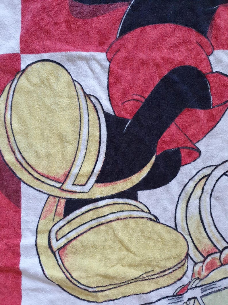 May include: A white, red, and black cartoon character towel. The towel features a cartoon character's yellow shoes with white trim, red shorts, and black arms. The background has a red and white checkered pattern.