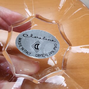 May include: Close-up of a clear glass bowl with a silver label that reads "Claraluna Made in Italy Crystal 24% PbO".