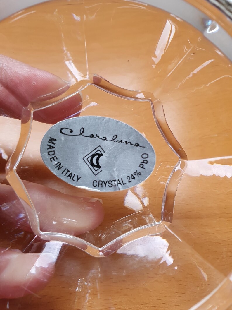May include: Close-up of a clear glass bowl with a silver label that reads "Claraluna Made in Italy Crystal 24% PbO".