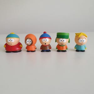 Op de afbeelding: Een set van vijf South Park-figuurtjes die in een rij staan. De figuren zijn Eric Cartman in een rode jas, Kenny McCormick in een oranje parka, Stan Marsh met een blauwe muts, Kyle Broflovski met een groene muts en Butters Stotch in een blauw shirt.
