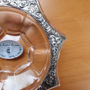 May include: A clear glass dish with a silver rim and a decorative design. The dish has a label that reads "Bareluno Italy Crystal 24% PbO".