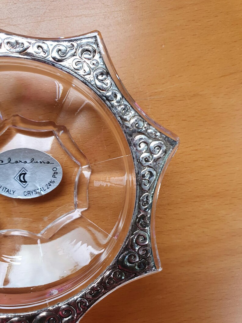 May include: A clear glass dish with a silver rim and a decorative design. The dish has a label that reads "Bareluno Italy Crystal 24% PbO".
