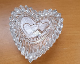 Può includere: Una scatola portaoggetti in vetro trasparente a forma di cuore con un design testurizzato dettagliato. La scatola presenta due cuori più piccoli all'interno, creando un effetto a strati.