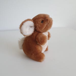 May include: A plush toy rabbit with soft brown fur, featuring a white chest, white inner ears, and a small white tail. The stuffed animal has dark plastic eyes, a small nose, and whiskers, standing in an upright position with rounded limbs.