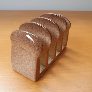 以下が含まれることがあります： パンの形をしたセラミック製のパンラック。ラックは茶色で斑点模様の仕上げになっており、パンを置くためのスロットが4つあります。