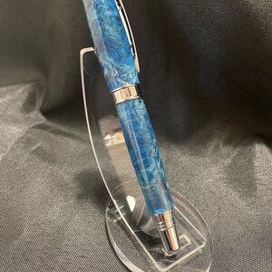 May include: A blue and silver pen with a wood grain pattern is displayed on a clear acrylic stand.