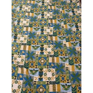 May include: A patchwork quilt with a repeating pattern of squares and rectangles. The quilt features a variety of colors, including blue, green, yellow, and white. The design includes floral and geometric shapes, and bird motifs.