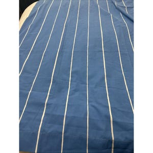 May include: Blue fabric with vertical white stripes. The stripes are evenly spaced and run the length of the fabric. The fabric appears to be a medium weight cotton or linen, suitable for curtains or other home decor projects.