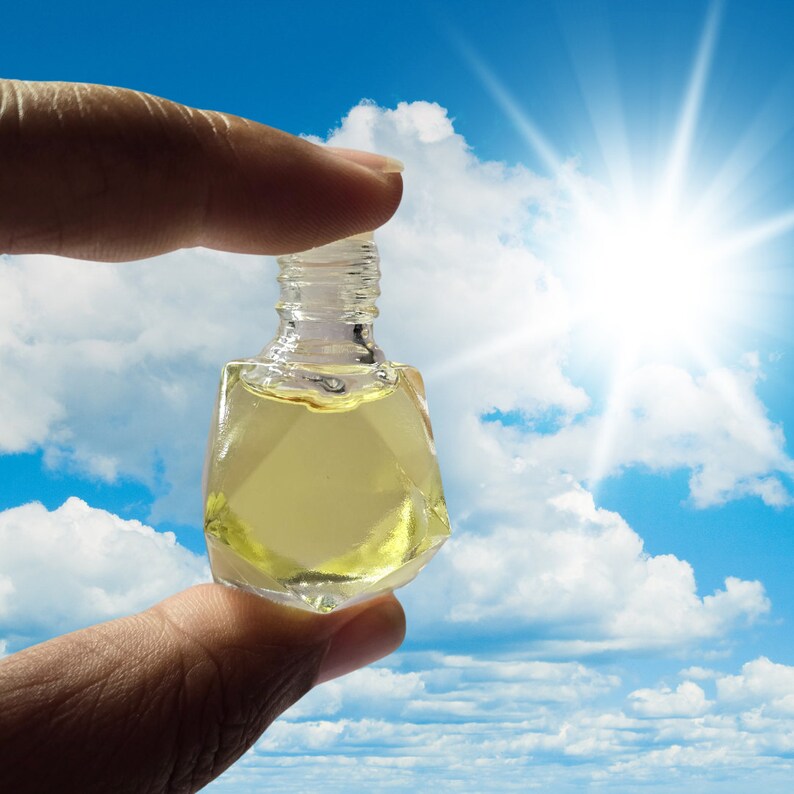 Puede incluir: Una botella de vidrio transparente con un l&iacute;quido amarillo en su interior, sostenida por una mano contra un cielo azul con nubes blancas y un sol brillante.