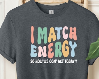 May include: A dark heather grey t-shirt with the text "I MATCH ENERGY SO HOW WE GON' ACT TODAY?" in colorful, bubble-like letters.