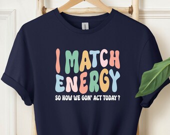May include: Navy blue t-shirt with the text "I MATCH ENERGY SO HOW WE GON' ACT TODAY?" in colorful, wavy letters.