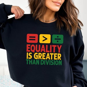 May include: Black sweatshirt with a graphic design featuring three colored squares with the symbols equals, greater than, and divided by. The text below the squares reads "Equality is greater than division".