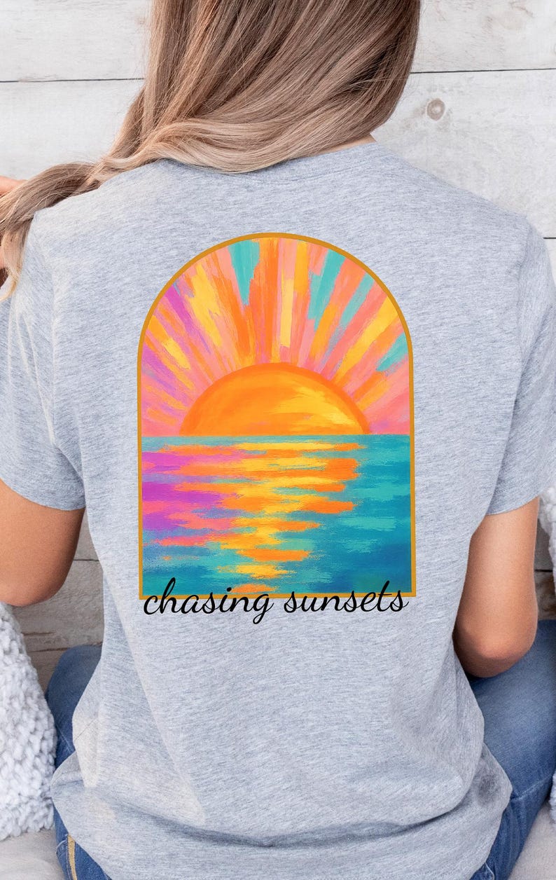 May include: A gray t-shirt with a colorful painting of a sunset over the ocean. The painting is in a gold arch shape. The text 'chasing sunsets' is below the painting.