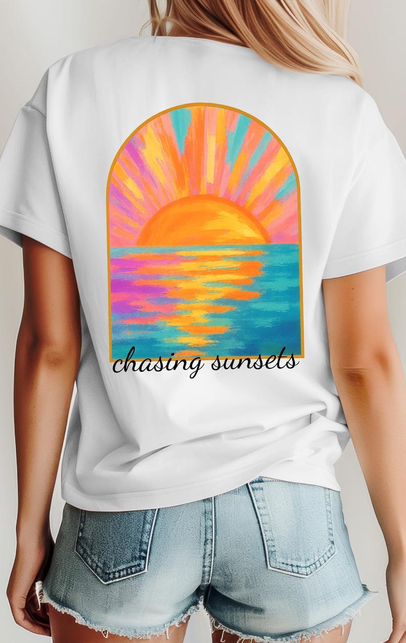 May include: White t-shirt featuring a colorful sunset design with the text "chasing sunsets." The graphic depicts a vibrant orange sun setting over a blue ocean, with pink, orange, and yellow hues. The shirt is a casual wear item.