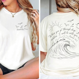 May include: Cream-colored t-shirt with a black graphic of seagulls and the text "Isaiah 43:2" on the front. The back features a sun, seagulls, a wave, and the quote "When you go through deep waters. I will be with you. Isaiah 43:2."