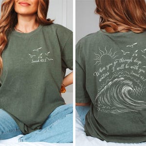 May include: Olive green t-shirt with white graphic of birds and text "Isaiah 43:2" on the front. The back features a sun, birds, wave design, and the text "When you go through deep waters, I will be with you. Isaiah 43:2."