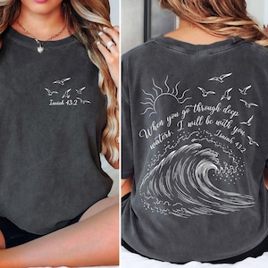 May include: Dark gray t-shirt with white graphic of birds and text "Isaiah 43:2" on the front. The back features a sun, birds, wave design, and the text "When you go through deep waters, I will be with you. Isaiah 43:2."