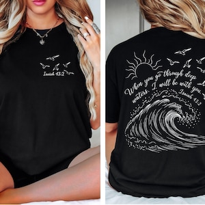 May include: Black t-shirt with white graphic text and illustrations. The front features flying birds and the text "Isaiah 43:2". The back displays a sun, birds, a wave, and the text "When you go through deep waters. I will be with you. Isaiah 43:2".